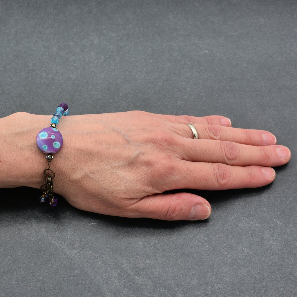 Hand wearing a bracelet with a purple bead on a gray background