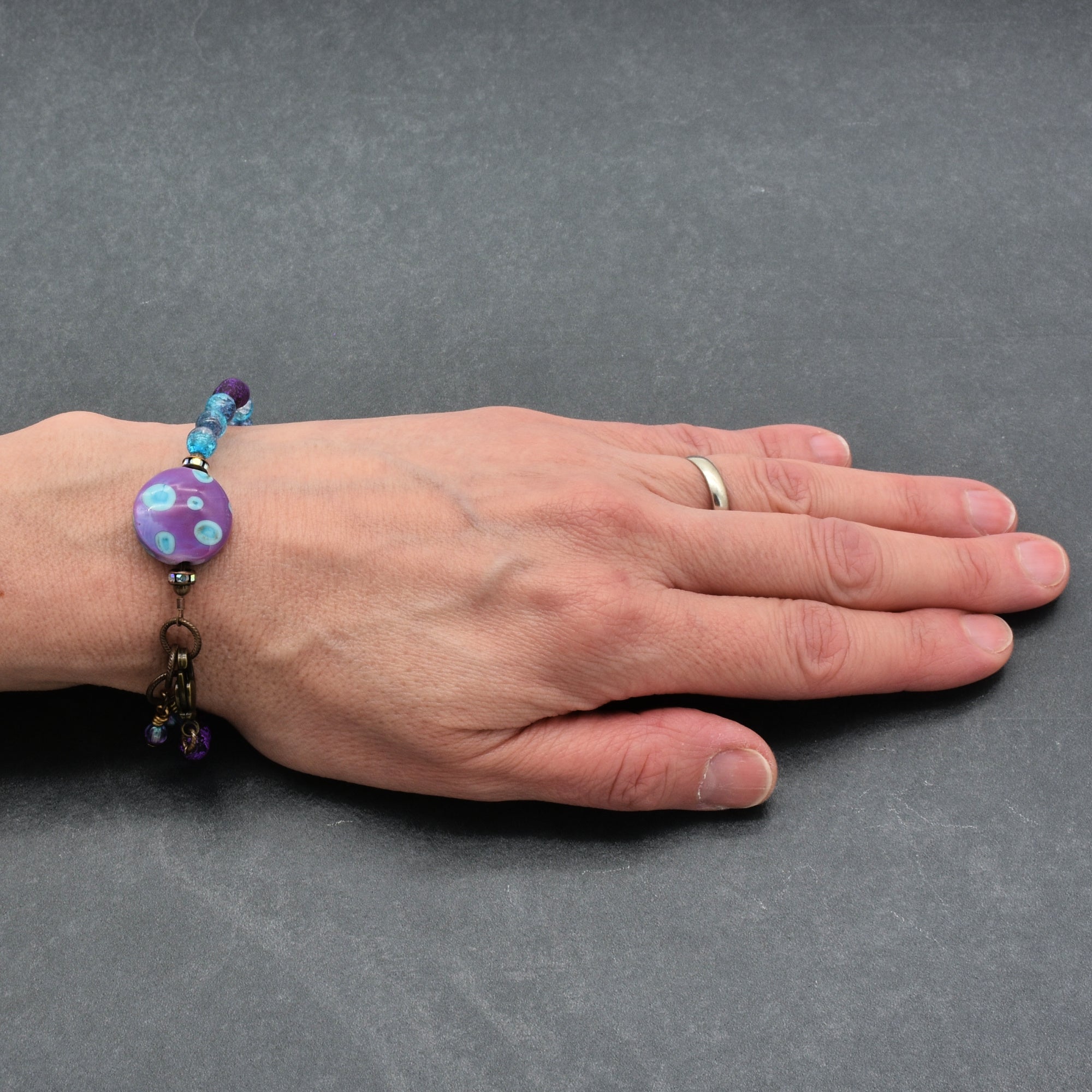 Hand wearing a bracelet with a purple bead on a gray background