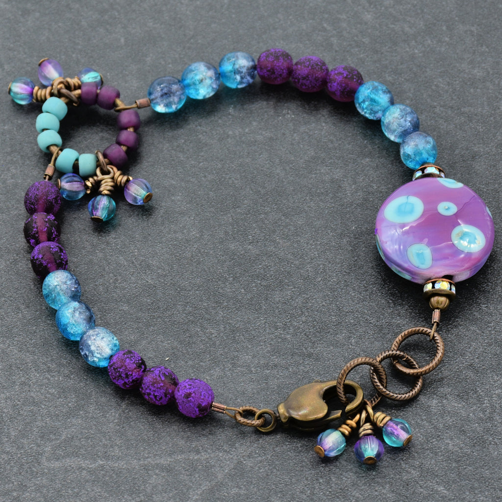 Multicolored beaded bracelet with a purple and blue polka dotted-patterned bead on a gray background
