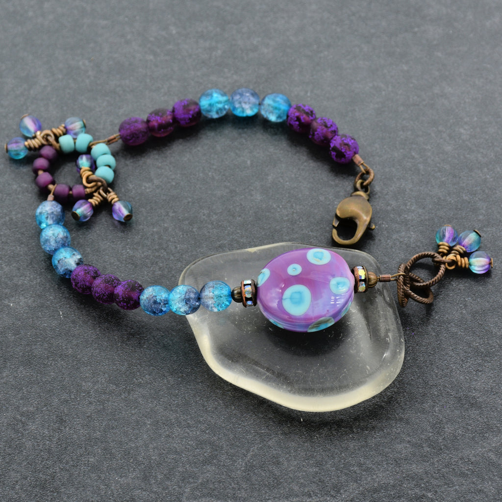 Beaded bracelet with a purple and blue polka dotted lampwork bead on a gray surface