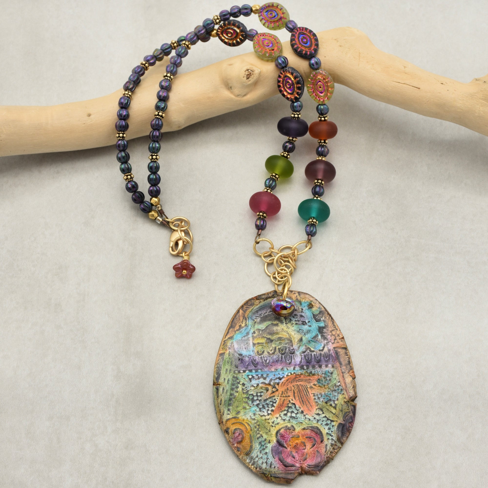 Colorful beaded necklace with a large, intricately designed pendant on a light gray background.