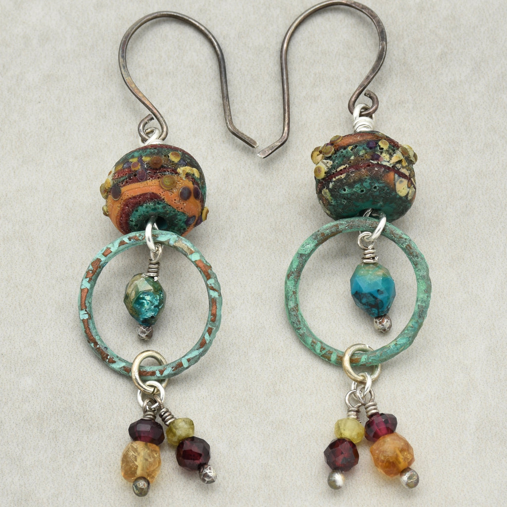 Unique autumn tone handmade pair of earrings with artisan lampwork glass, chrysocolla, green garnet, red garnet, purple garnet, citrine, oxidized silver ear wires, and artisan patinated turquoise rings on a light gray background