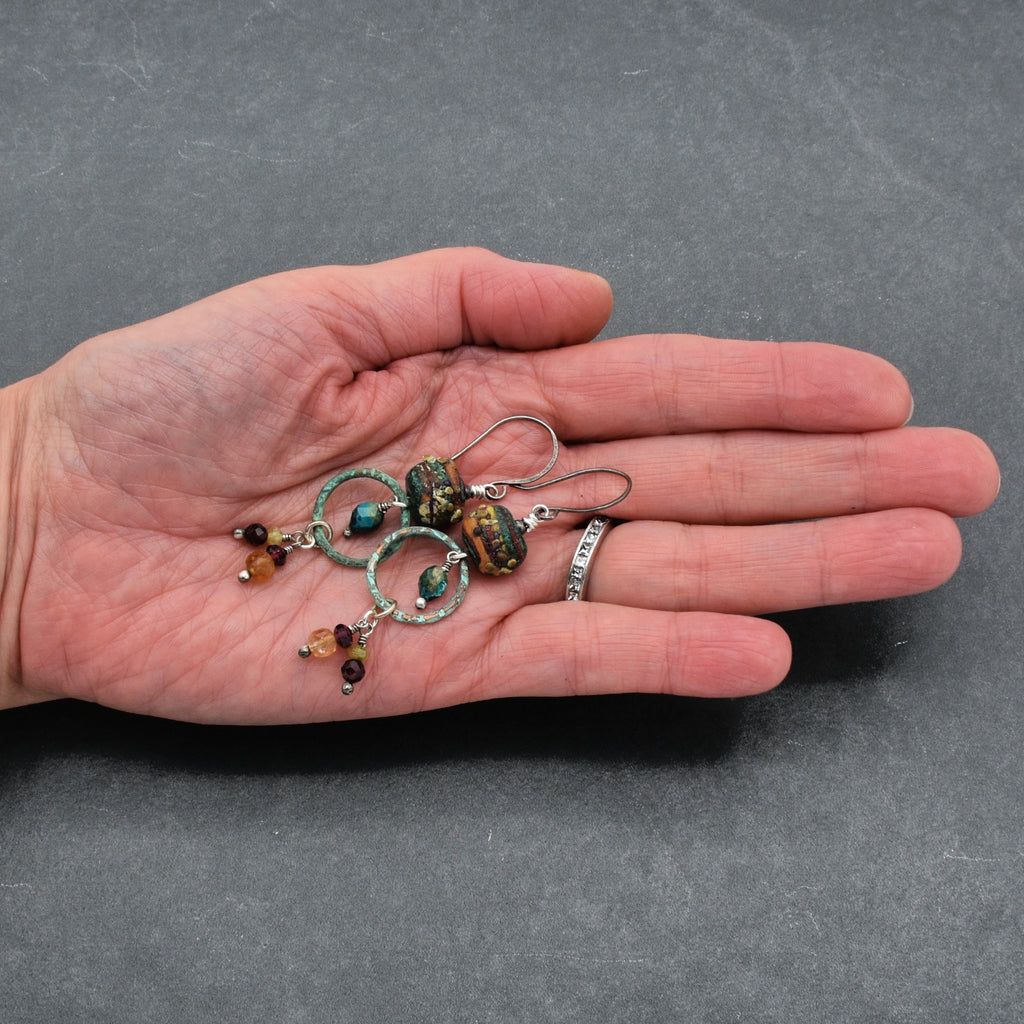 Hand holding Autumn Berries earrings with a gray background