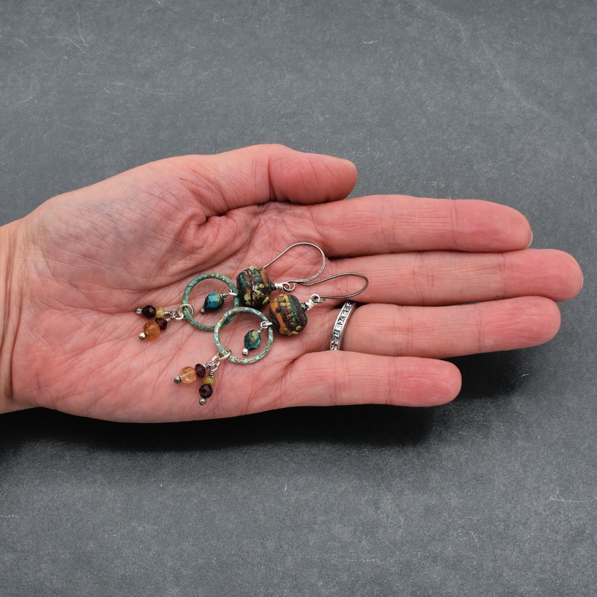 Hand holding Autumn Berries earrings with a gray background