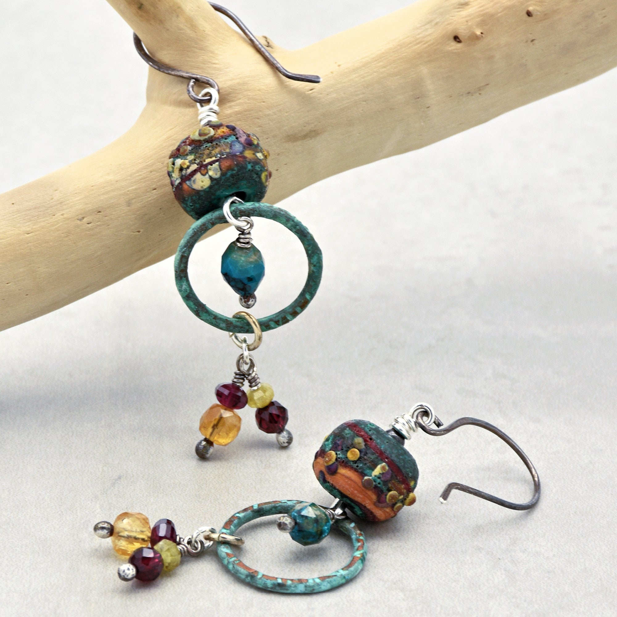 Colorful beaded earrings on a wooden branch against a white background