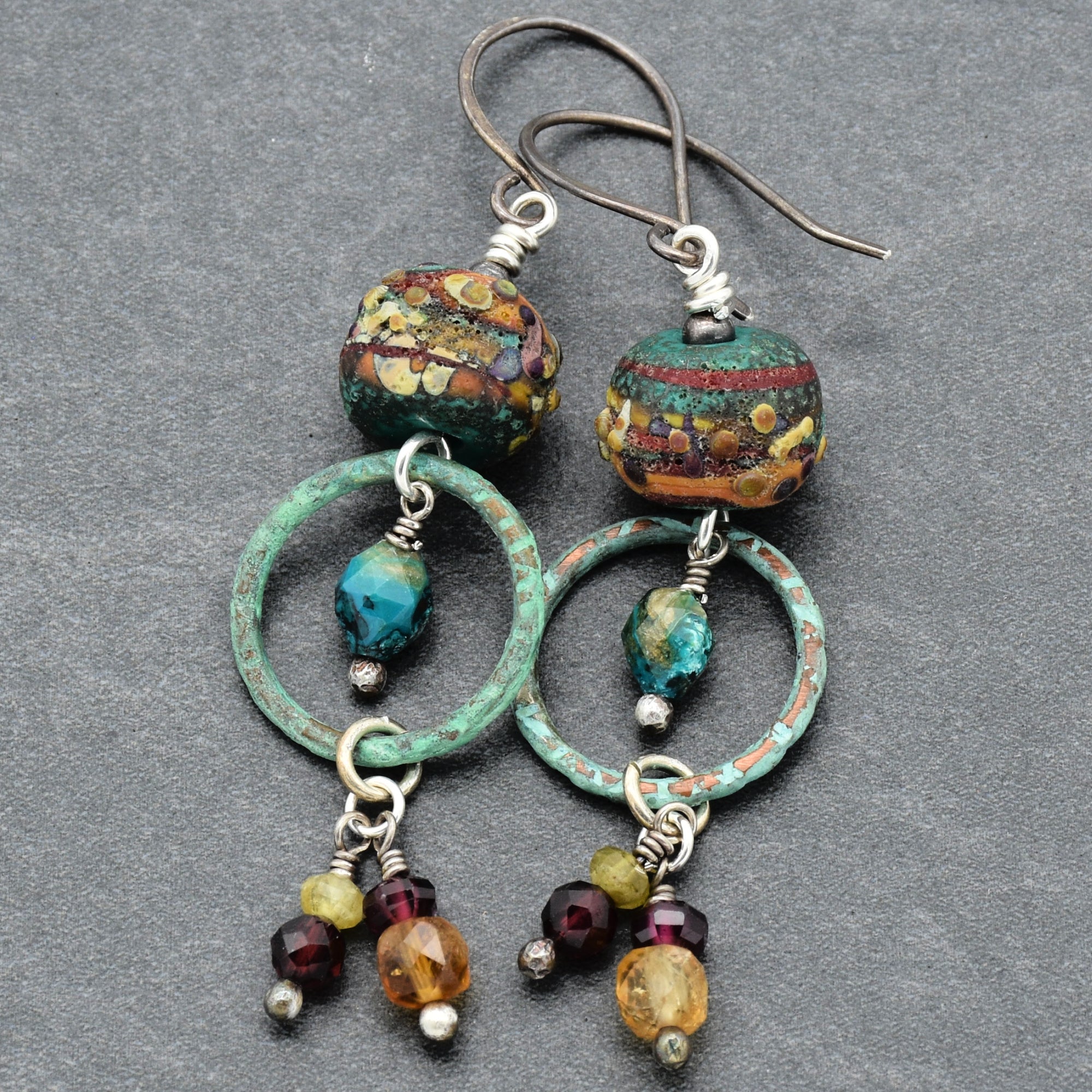 Colorful handmade beaded earrings with artisan lampwork glass, Chrysocolla, red and green garnet, citrine and oxidized silver on a gray background