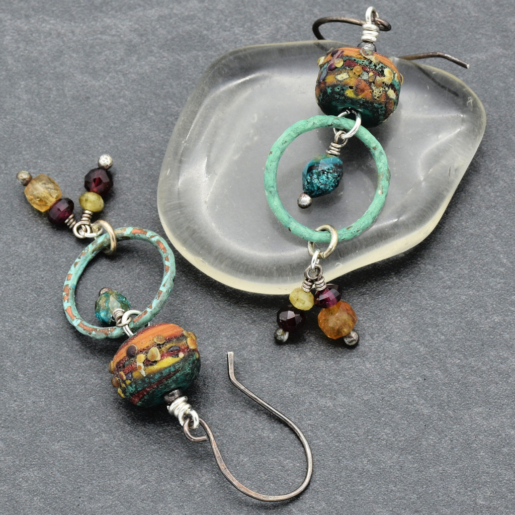 Pair of autumn color beaded earrings with garnet, artisan lampwork glass, chrysocolla, citrine and oxidized silver ear wires on a gray surface