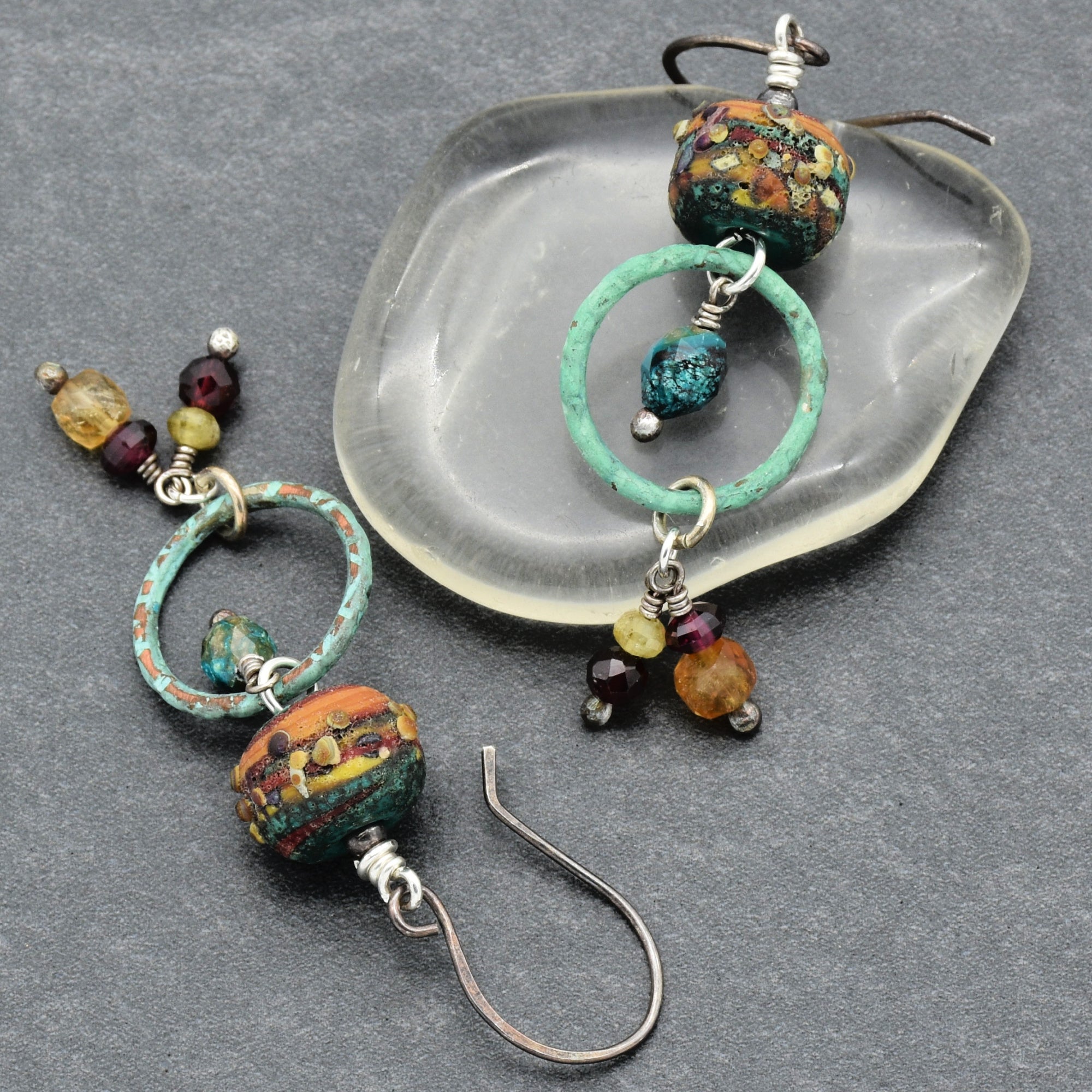 Pair of autumn color beaded earrings with garnet, artisan lampwork glass, chrysocolla, citrine and oxidized silver ear wires on a gray surface