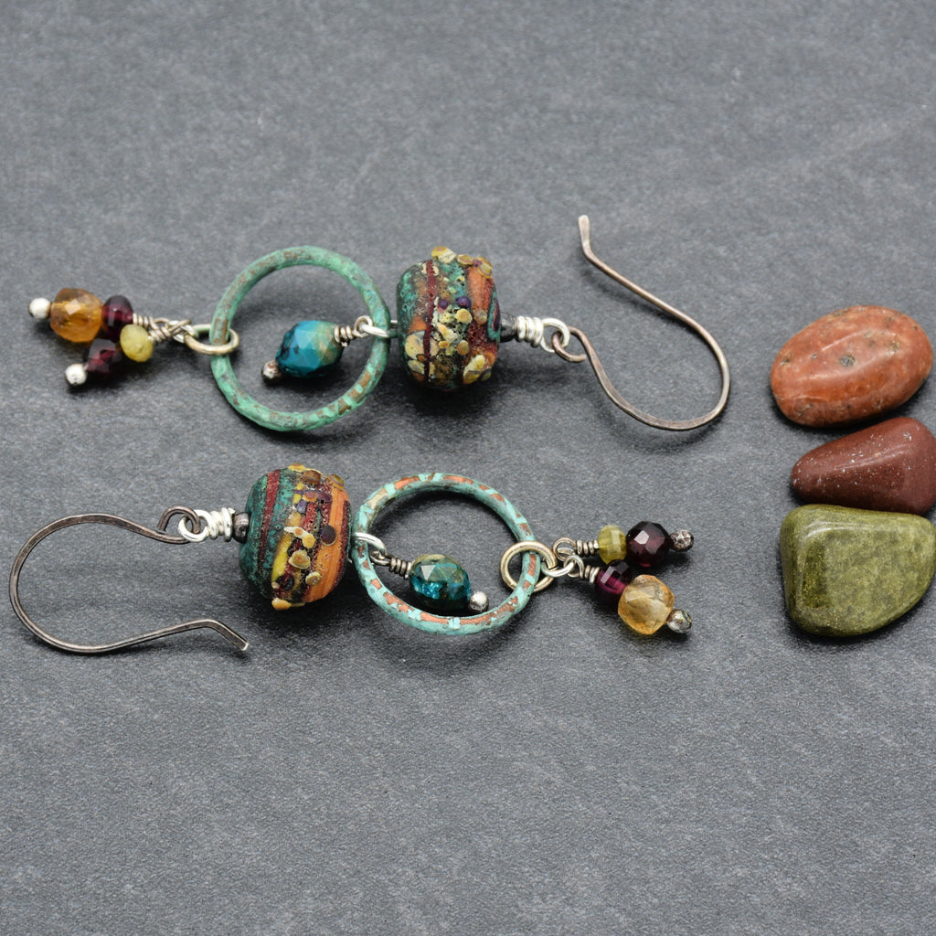 Pair of earrings with autumn color beads like turquoise, maroon, olive green, and golden yellow with oxidized silver ear wires on a gray surface