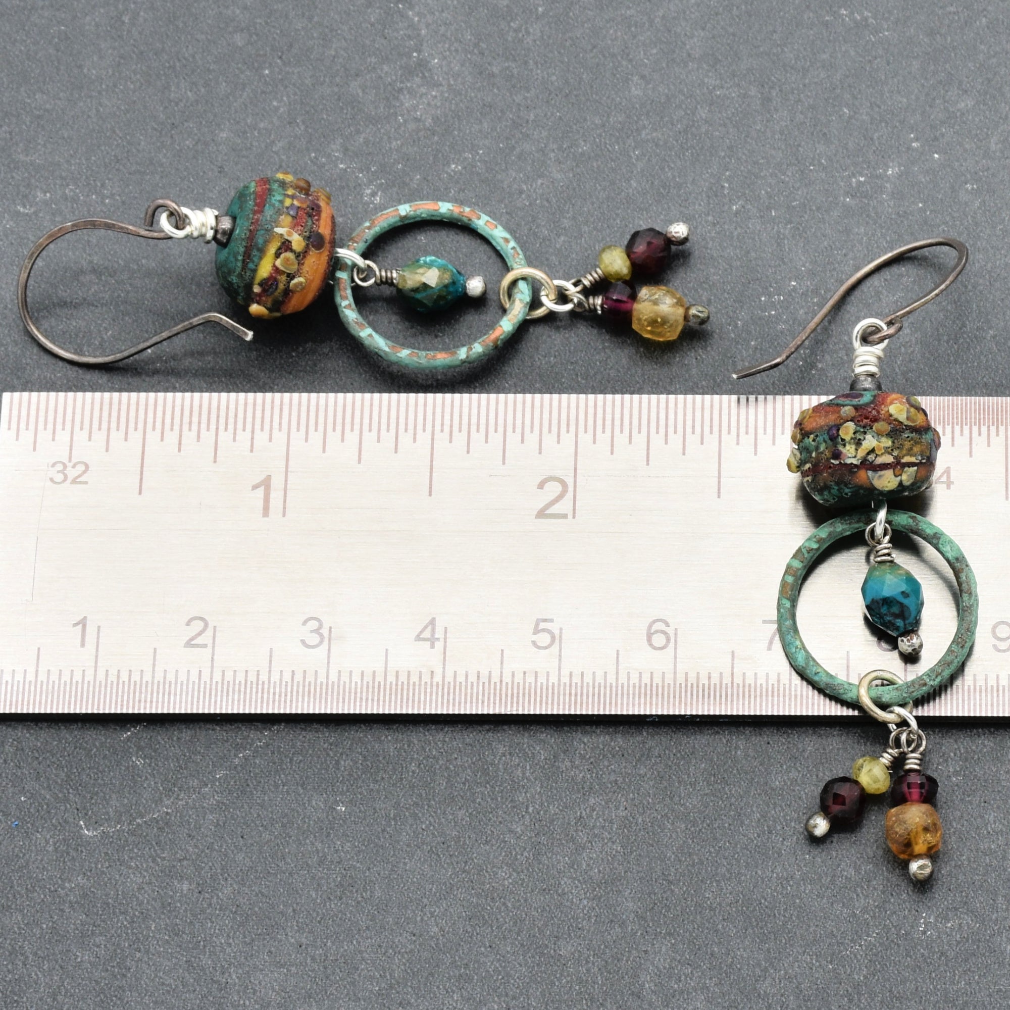Autumn Berries earrings on a ruler for scale, against a gray background