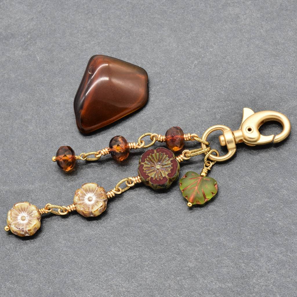 Harvest Bloom Handbag Charm featuring wire-wrapped rust hibiscus flowers and olive green maple leaf charm, handmade by Ruby Acorn