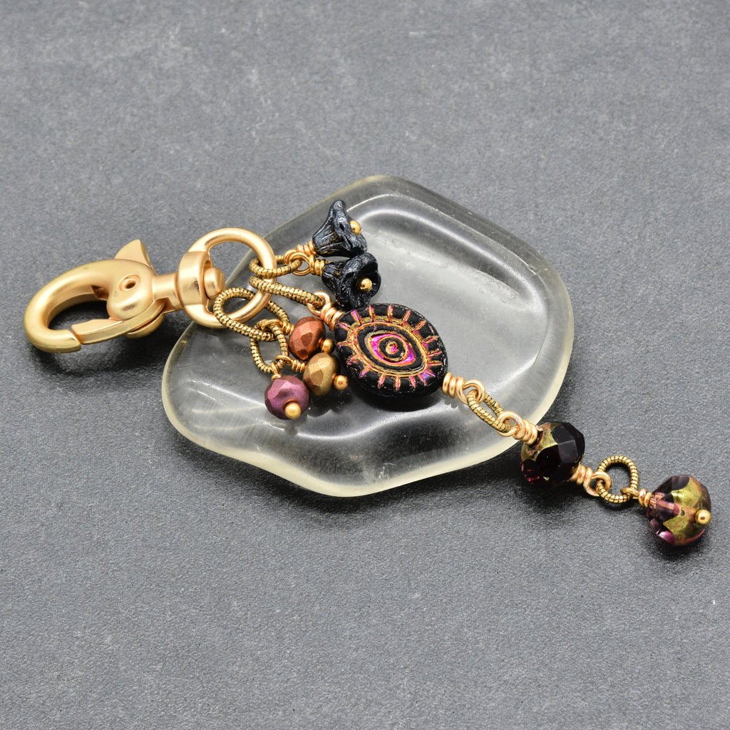 Ember Eye Handbag Charm featuring a graphite gray Czech glass evil eye focal with shimmery copper center, handmade by Ruby Acorn