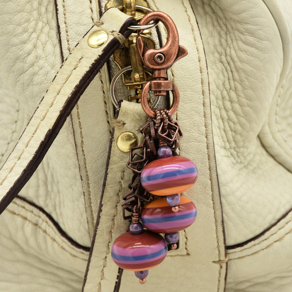 Close-up of a cream-colored leather purse featuring a decorative keychain charm with copper-toned hardware, purple beads, and striped vintage Lucite beads in pink, orange, and blue - made with love in Colorado by Ruby Acorn.