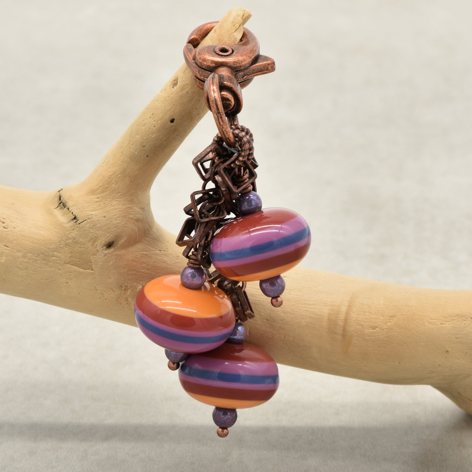 A handbag charm with three striped vintage Lucite beads in orange, purple, and blue, displayed on a light wood branch against a neutral gray background - made with love in Colorado by Ruby Acorn.