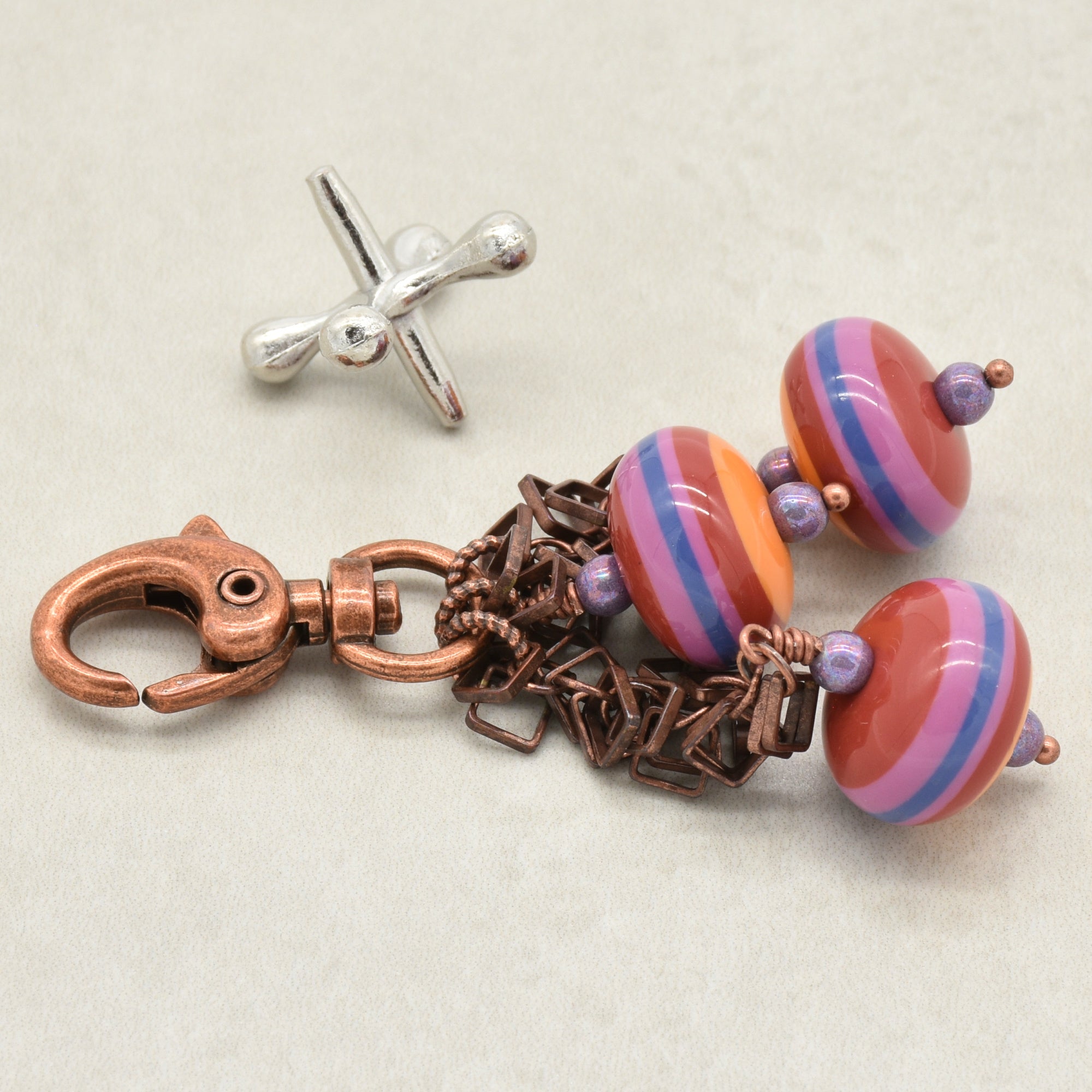 A handbag charm with colorful striped vintage Lucite beads in pink, orange, and blue, attached to a copper-toned chain with a lobster clasp, shown next to a silver jack on a light gray background - made with love in Colorado by Ruby Acorn.