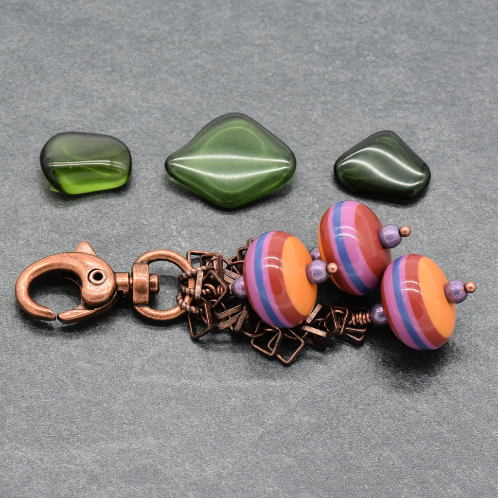 A keychain charm set on a gray textured background, three vintage Lucite striped beads in orange, pink, and blue with purple spacers, and a copper clasp and chain - made with love in Colorado by Ruby Acorn.