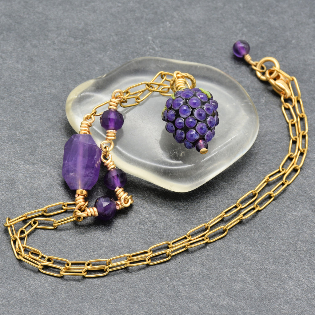 Asymmetrical gold chain necklace with artisan lampwork glass blackberry focal and amethyst on a gray background - handmade with love by Ruby Acorn