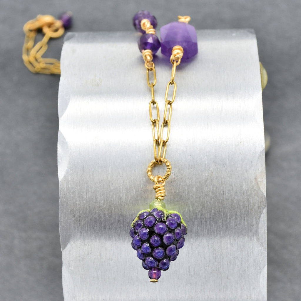 Closeup of asymmetrical gold chain necklace with artisan lampwork glass blackberry focal and amethyst on a silver background - handmade with love by Ruby Acorn