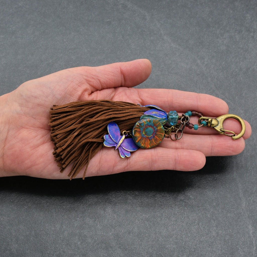 Hand holding a decorative keychain with tassel on a gray background