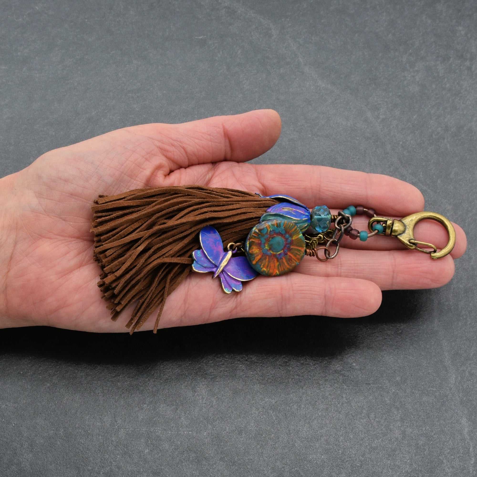 Hand holding a decorative keychain with tassel on a gray background