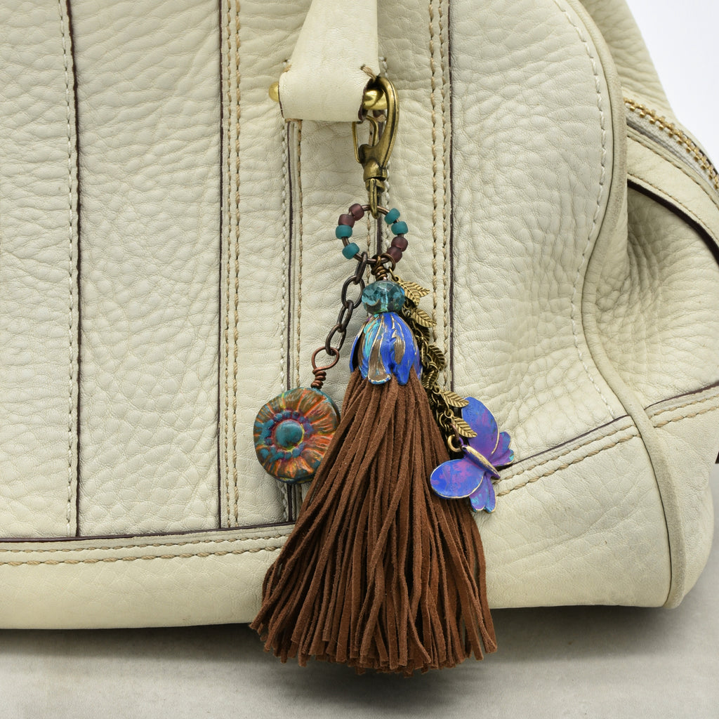 Decorative keychain with tassel and floral elements attached to a beige handbag.