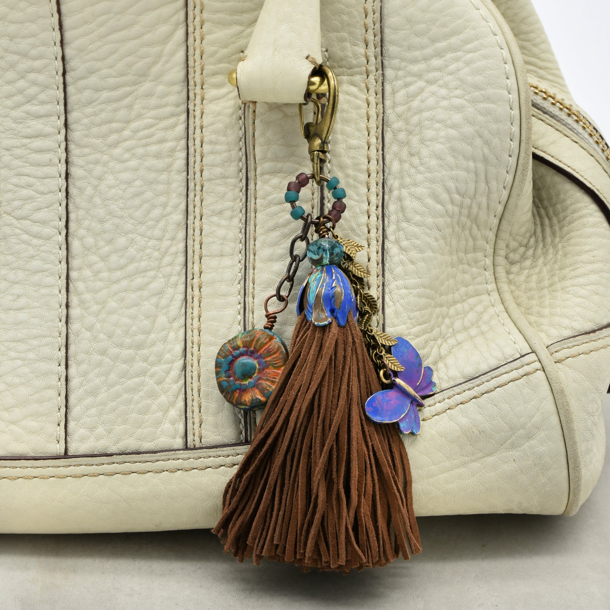 Decorative keychain with tassel and floral elements attached to a beige handbag.