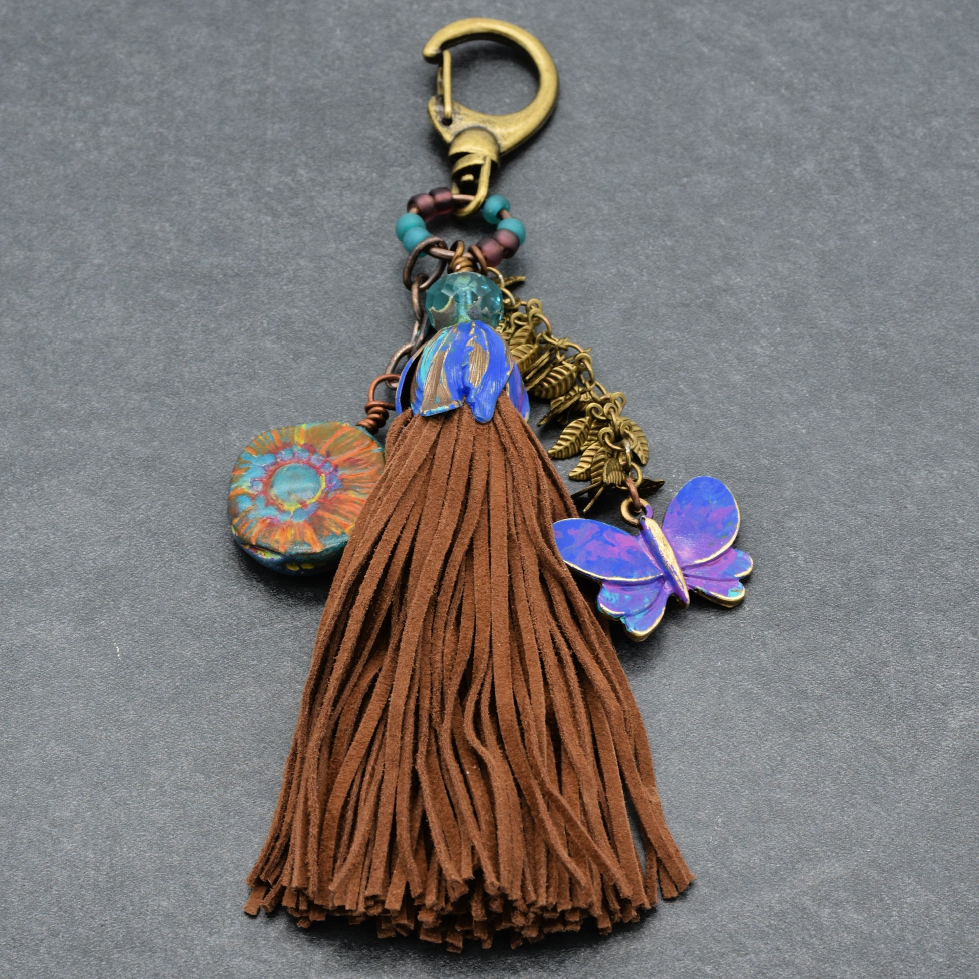 Decorative keychain with tassel, butterfly charm, and colorful accents on a gray background