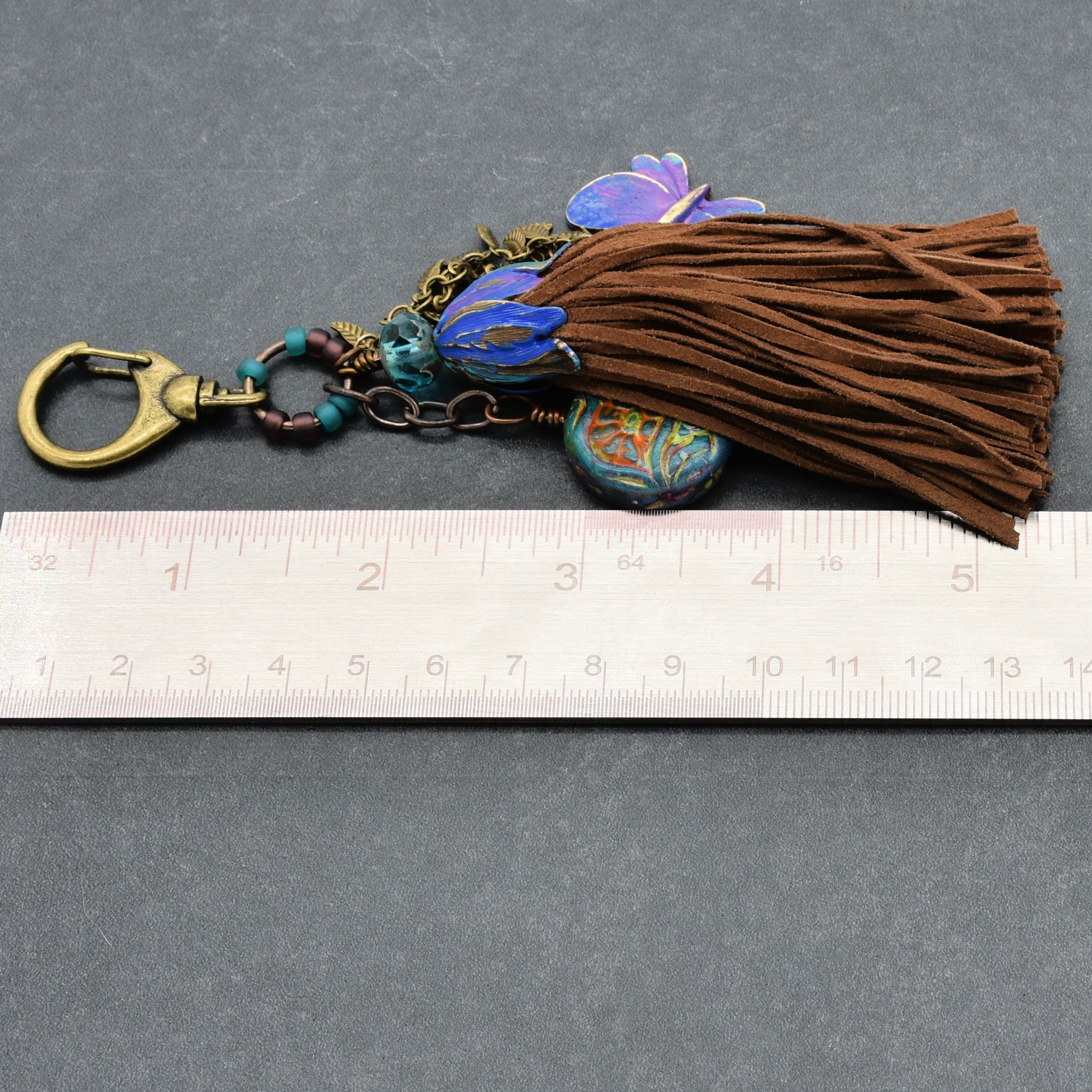Decorative keychain with tassel and floral elements on a gray background, measured against a ruler.