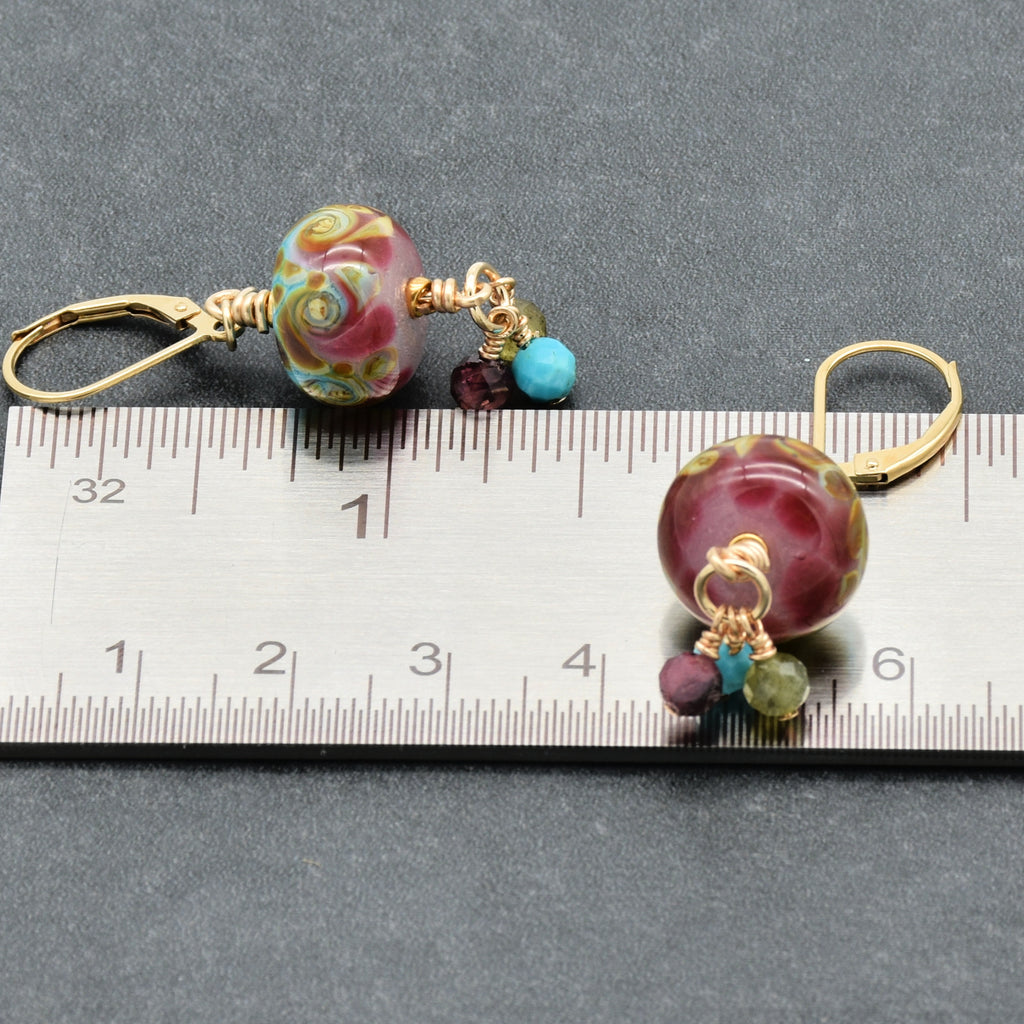 Colorful dangle earrings with charm shown on a ruler for scale