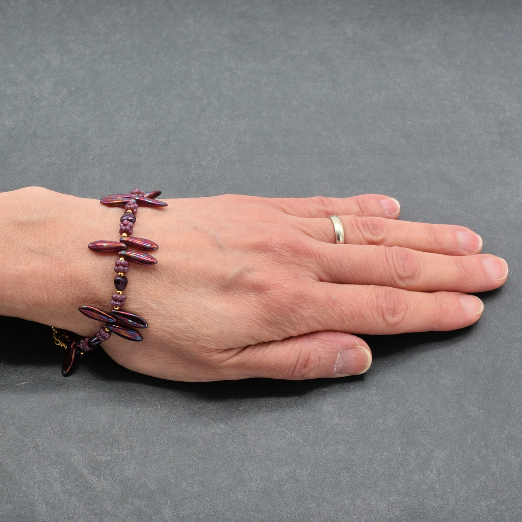 Hand wearing a burgundy beaded bracelet on a gray background