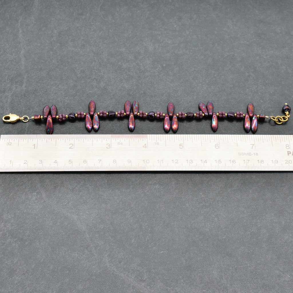 Bracelet with burgundy beads and gold clasp on a gray surface with a ruler for scale.
