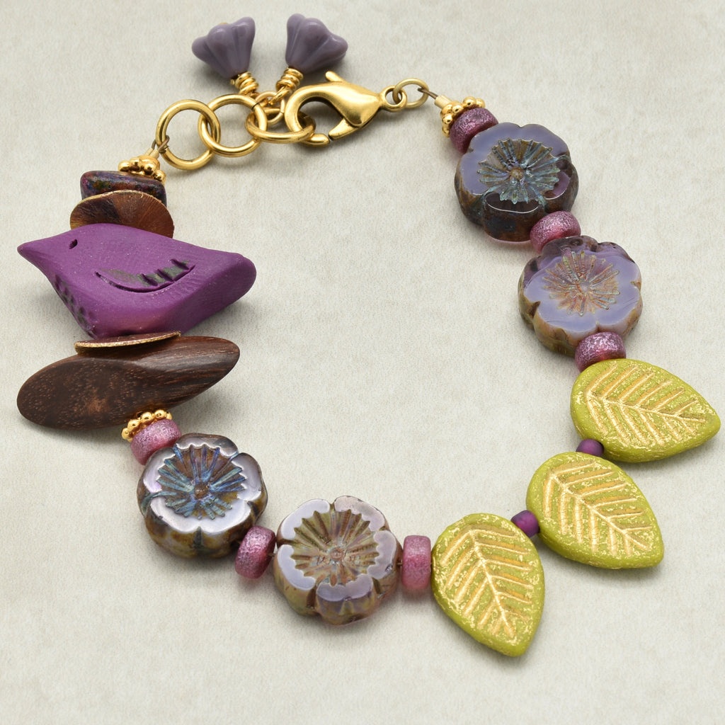 Colorful beaded bracelet with a bird focal and floral and leaf beads on a light background