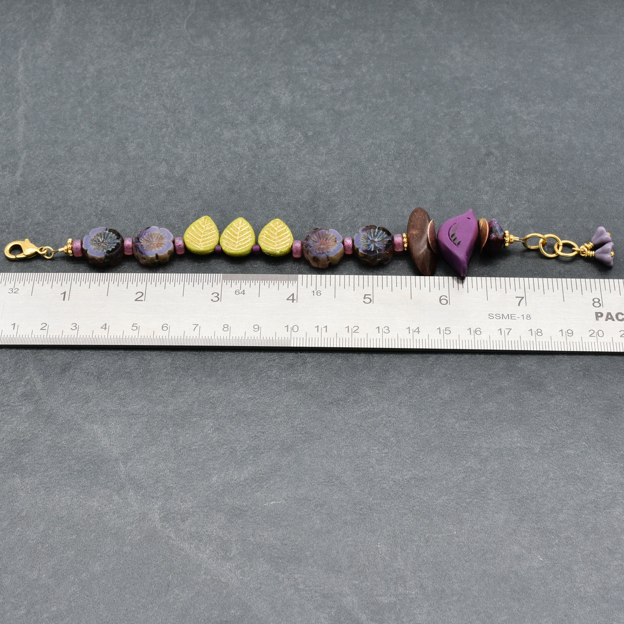 Beaded bracelet with gold clasps on a gray surface with a ruler for scale.