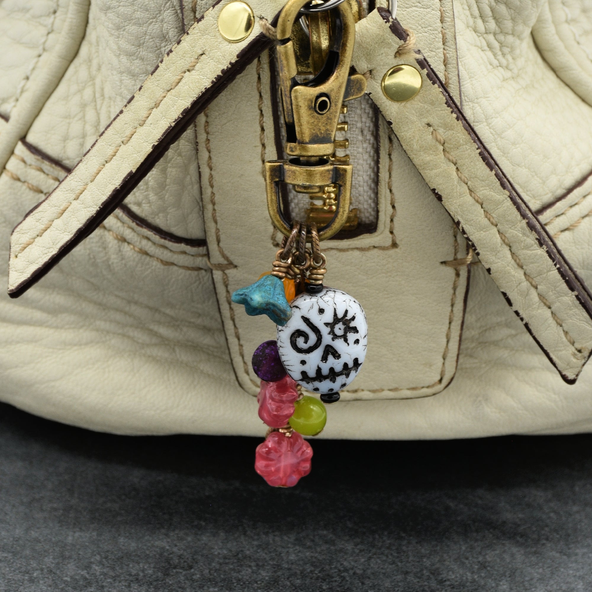 Colorful beaded keychain with skull design attached to a beige handbag.