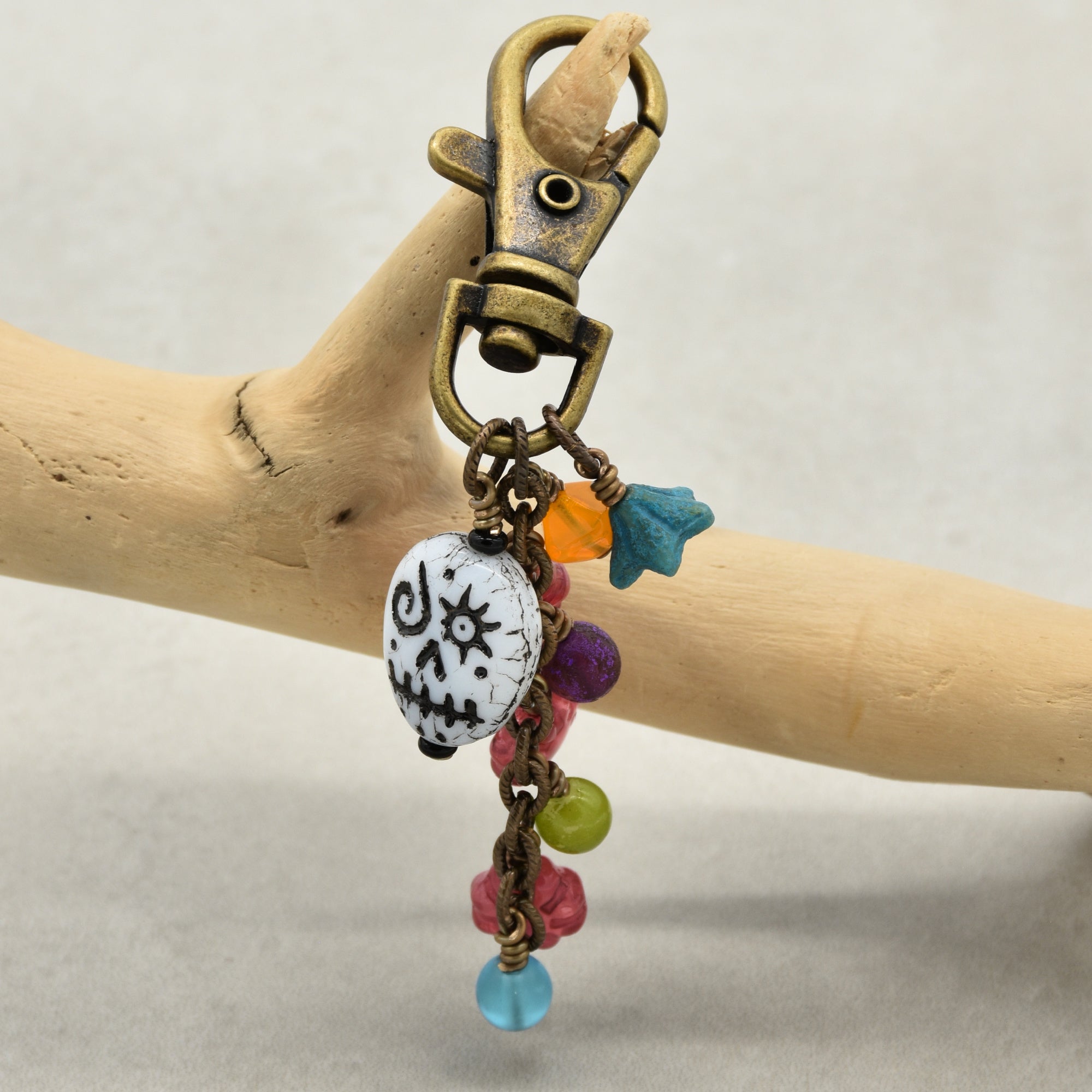 Colorful beaded keychain with a decorative skull charm on a wooden stick against a neutral background