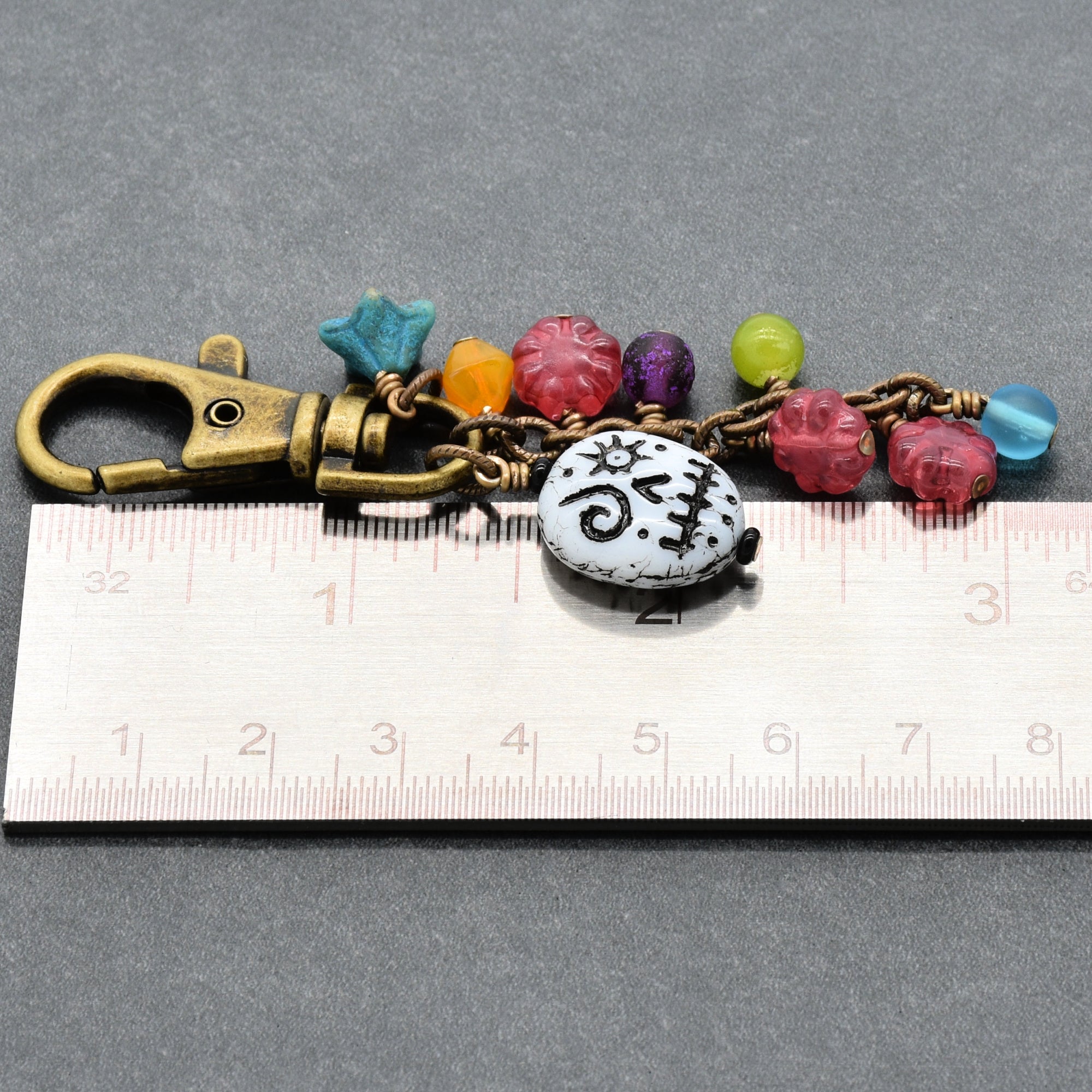 Keychain with colorful beads and a white button on a ruler for scale