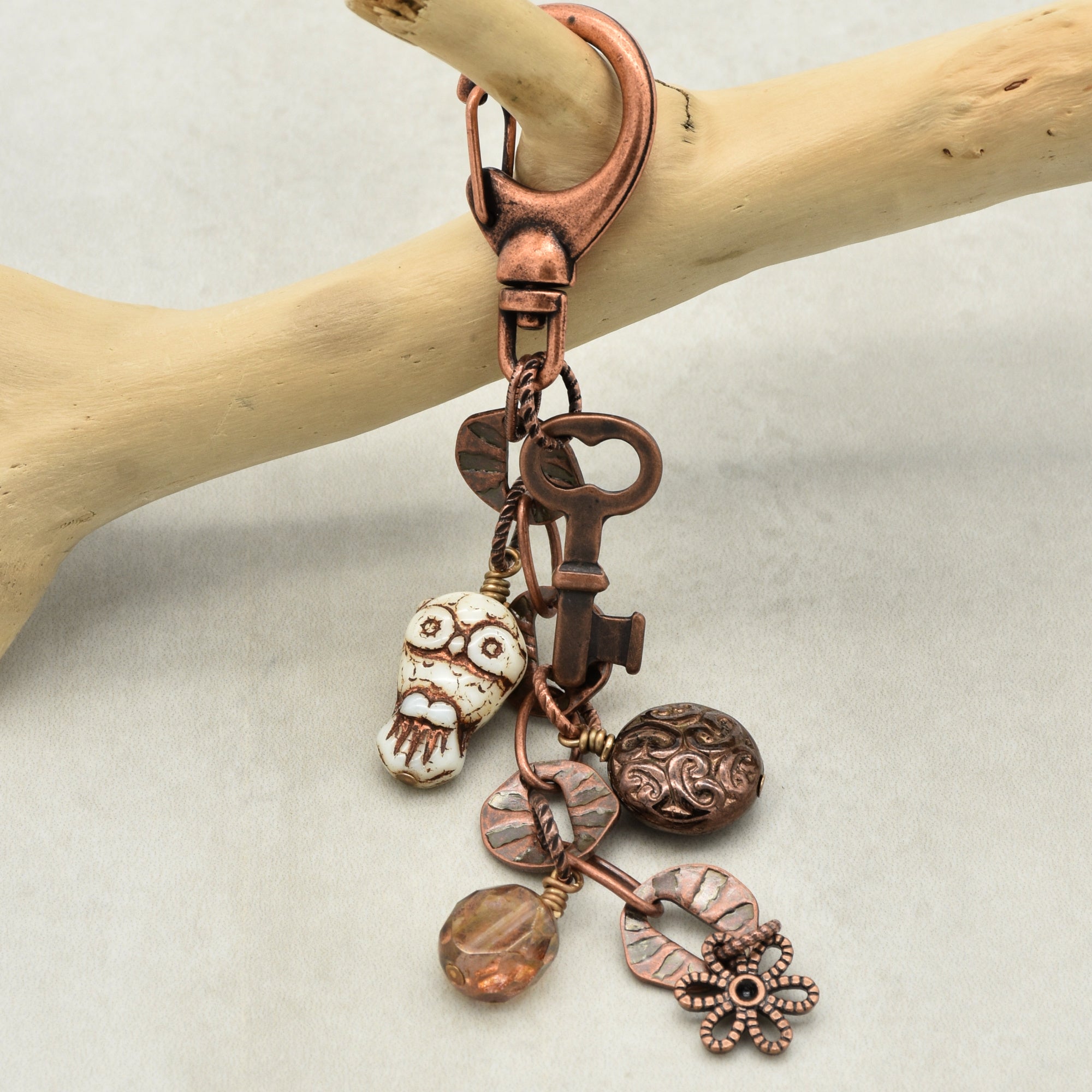 Copper keychain with various charms on a wooden branch