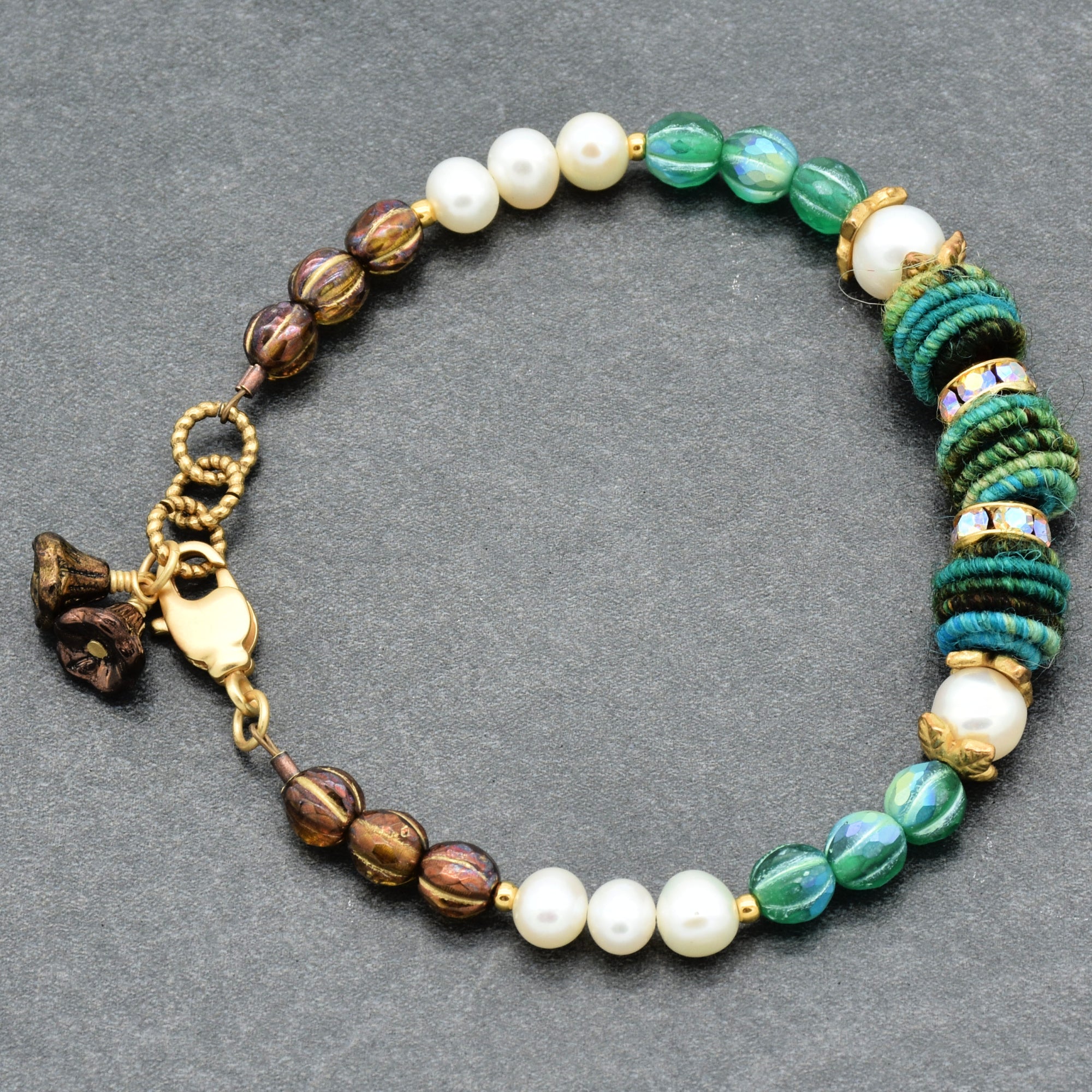 Beaded bracelet with pearls, green stones, and gold accents on a gray background