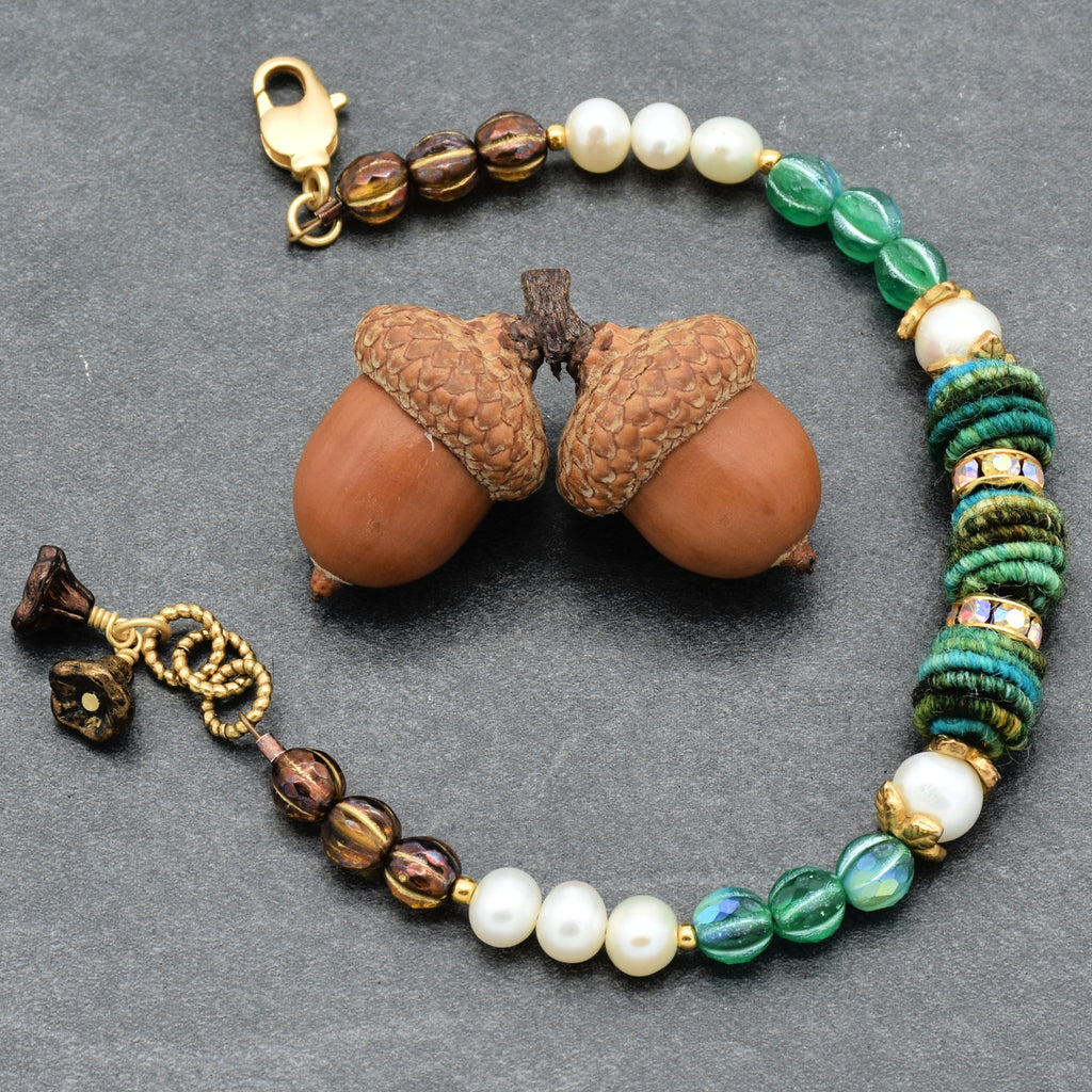 Beaded bracelet with pearls and green and brown beads on a gray surface