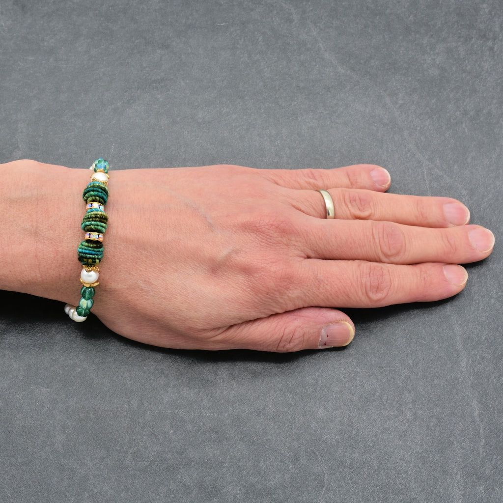 Hand wearing a beaded bracelet on a gray background