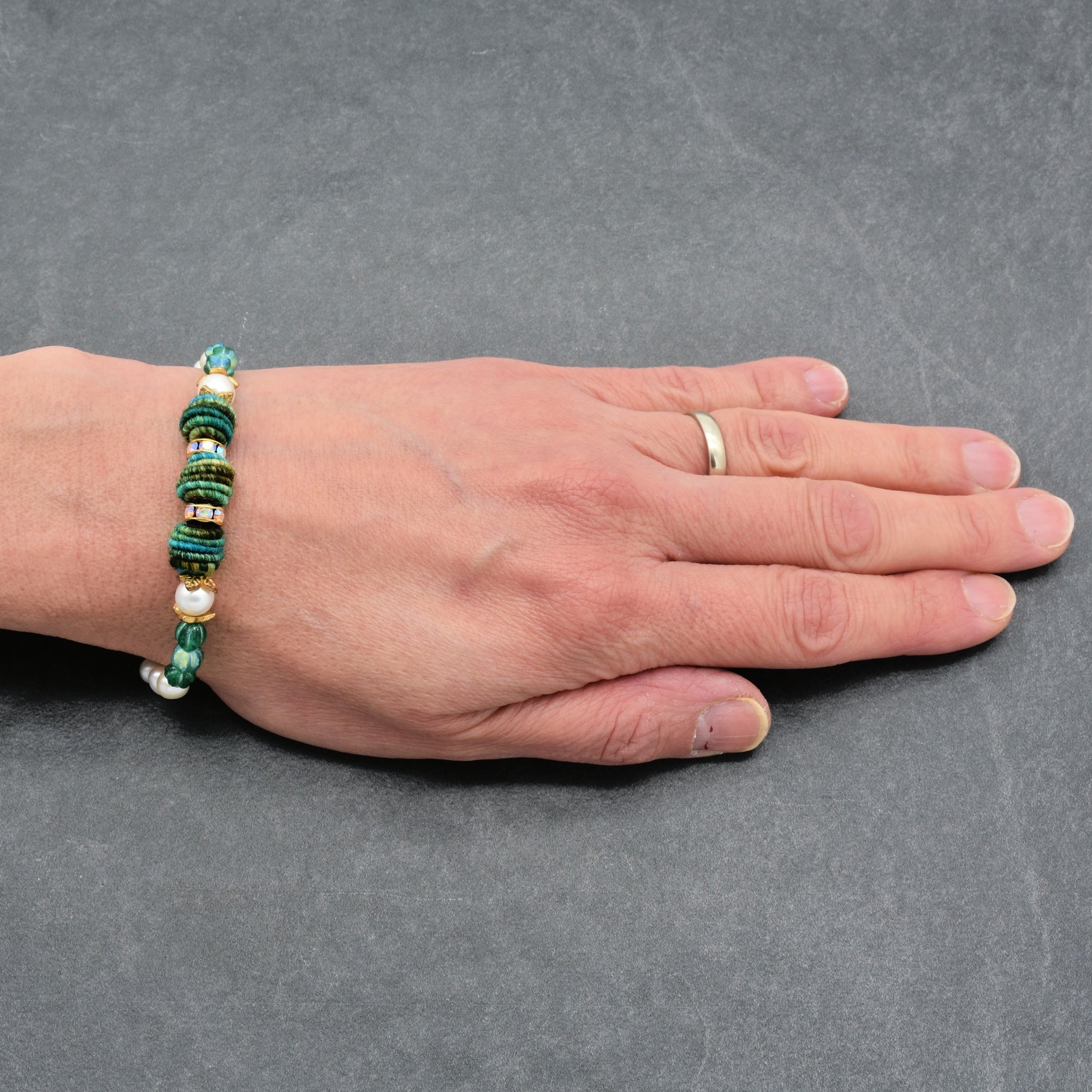 Hand wearing a beaded bracelet on a gray background