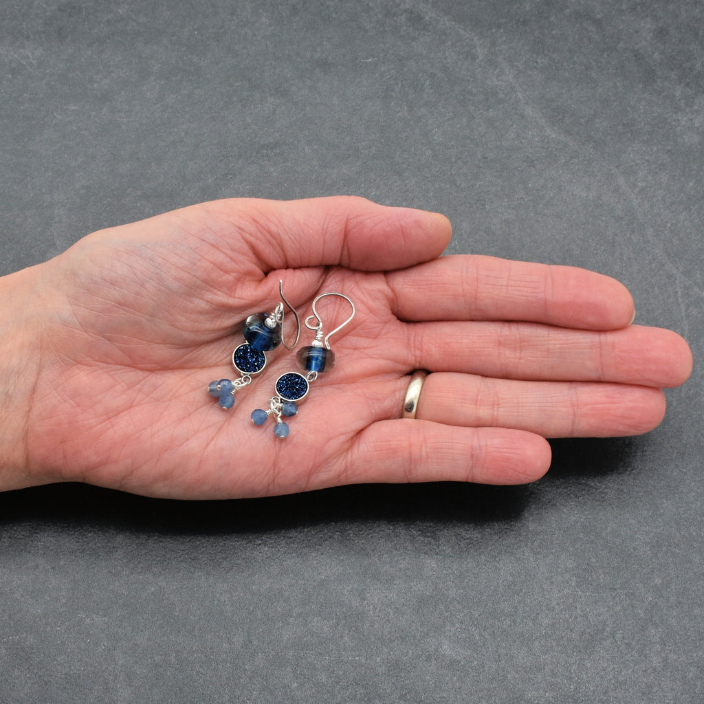 Hand holding a pair of blue beaded earrings against a gray background