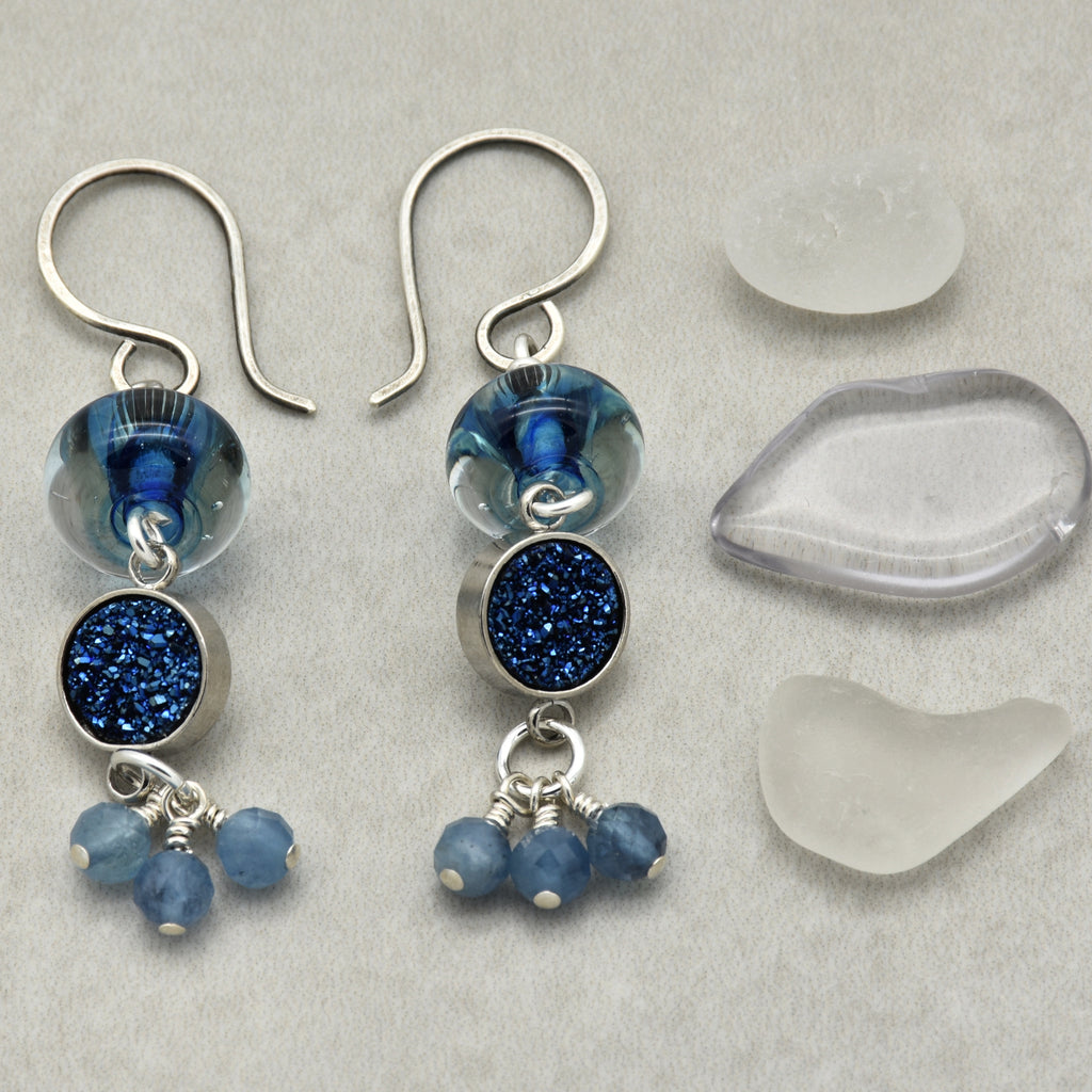 Pair of blue beaded earrings on a gray surface with clear stones.