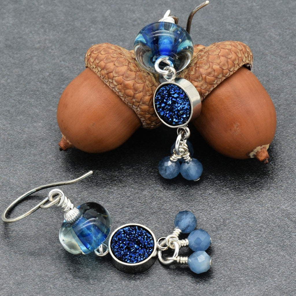 Blue beaded earrings with silver accents on a gray surface with acorns.