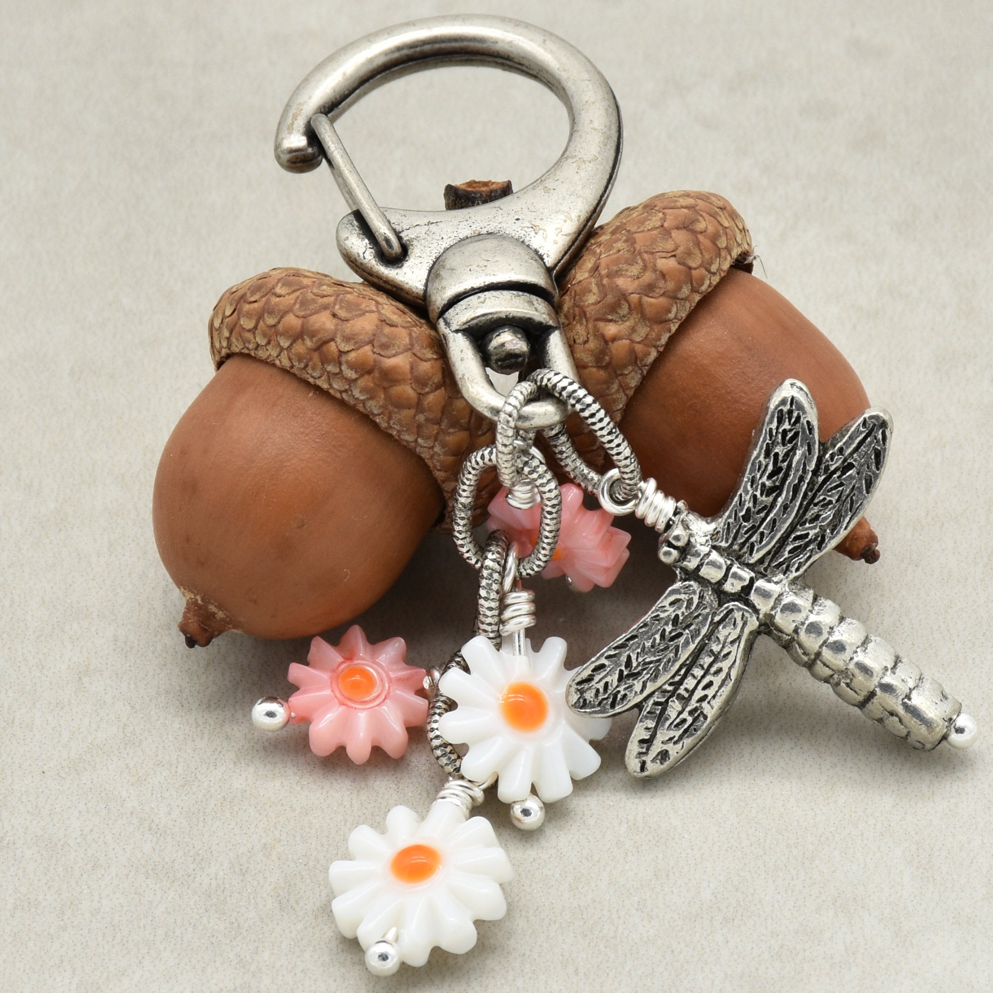 Silver keychain with flowers, and dragonfly charm on a beige background
