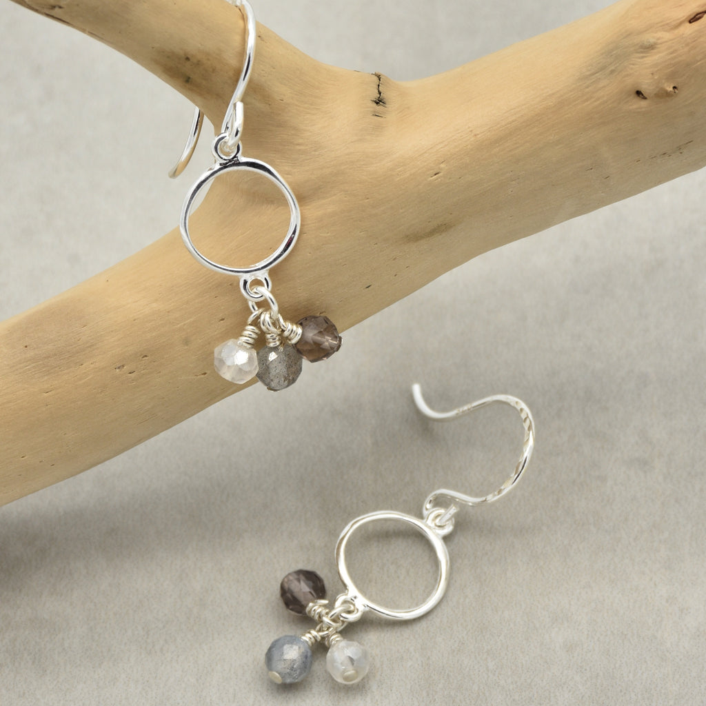 Silver earrings with gemstones on a wooden branch and gray background