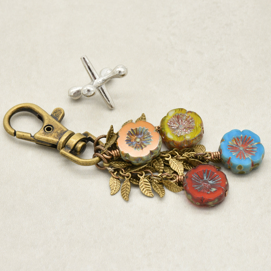 An antique bronze keychain with a lobster clasp and four colorful flower charms in orange, green, blue, and red, displayed on a light beige background - made with love in Colorado by Ruby Acorn.