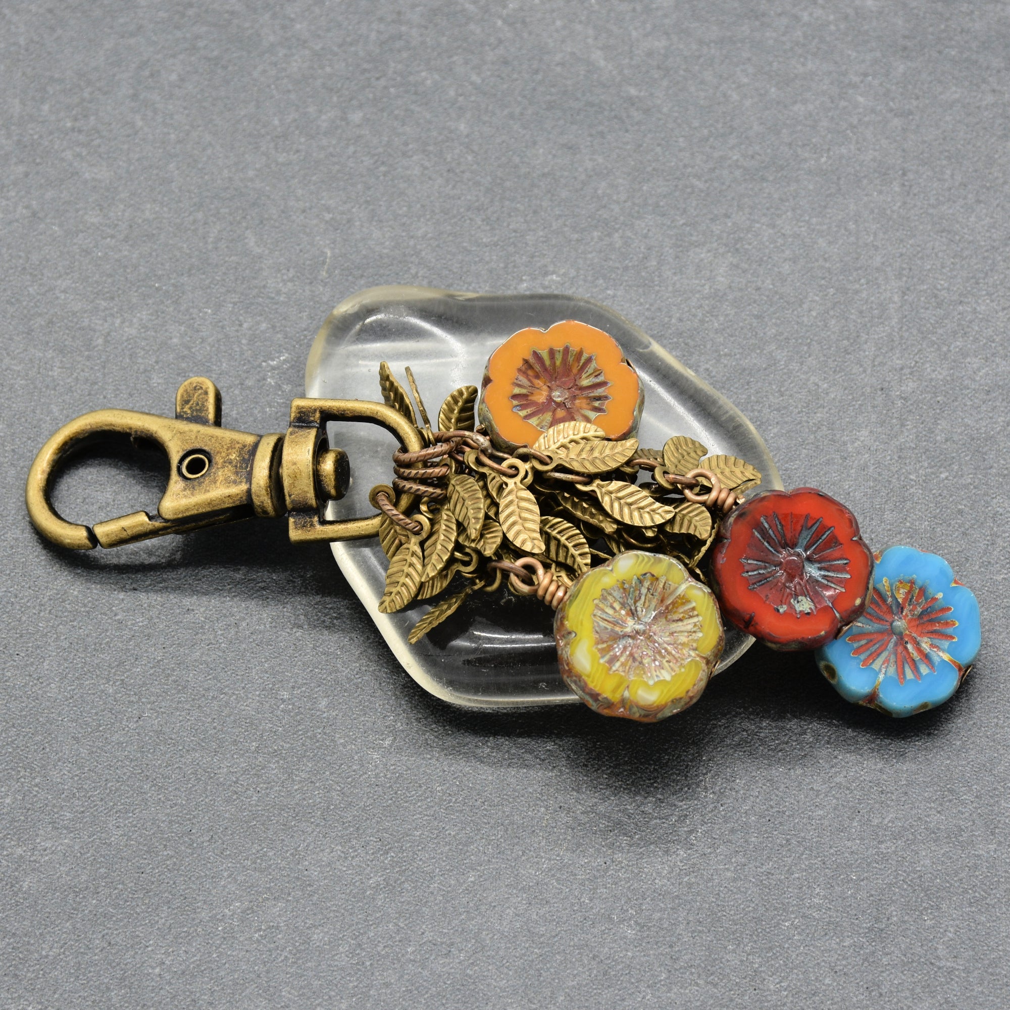 An antique bronze keychain featuring a lobster clasp and colorful flower charms in orange, red, yellow, and blue with metallic leaf details - made with love in Colorado by Ruby Acorn.
