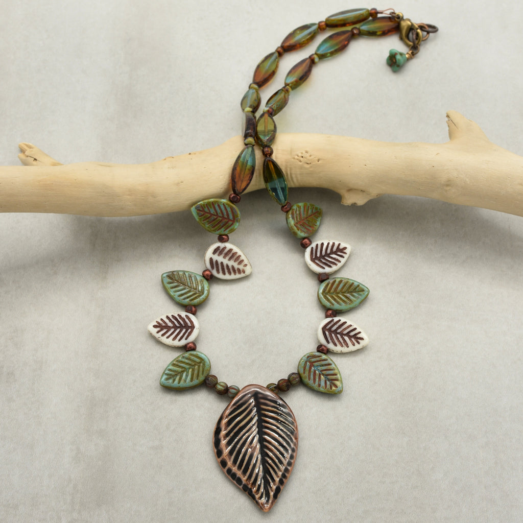 Necklace with leaf-shaped beads on a branch against a neutral background