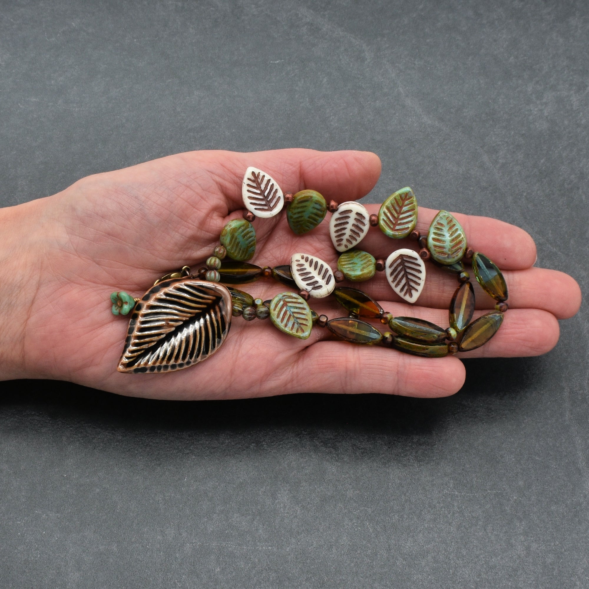 Hand holding a leaf-shaped necklace against a gray background